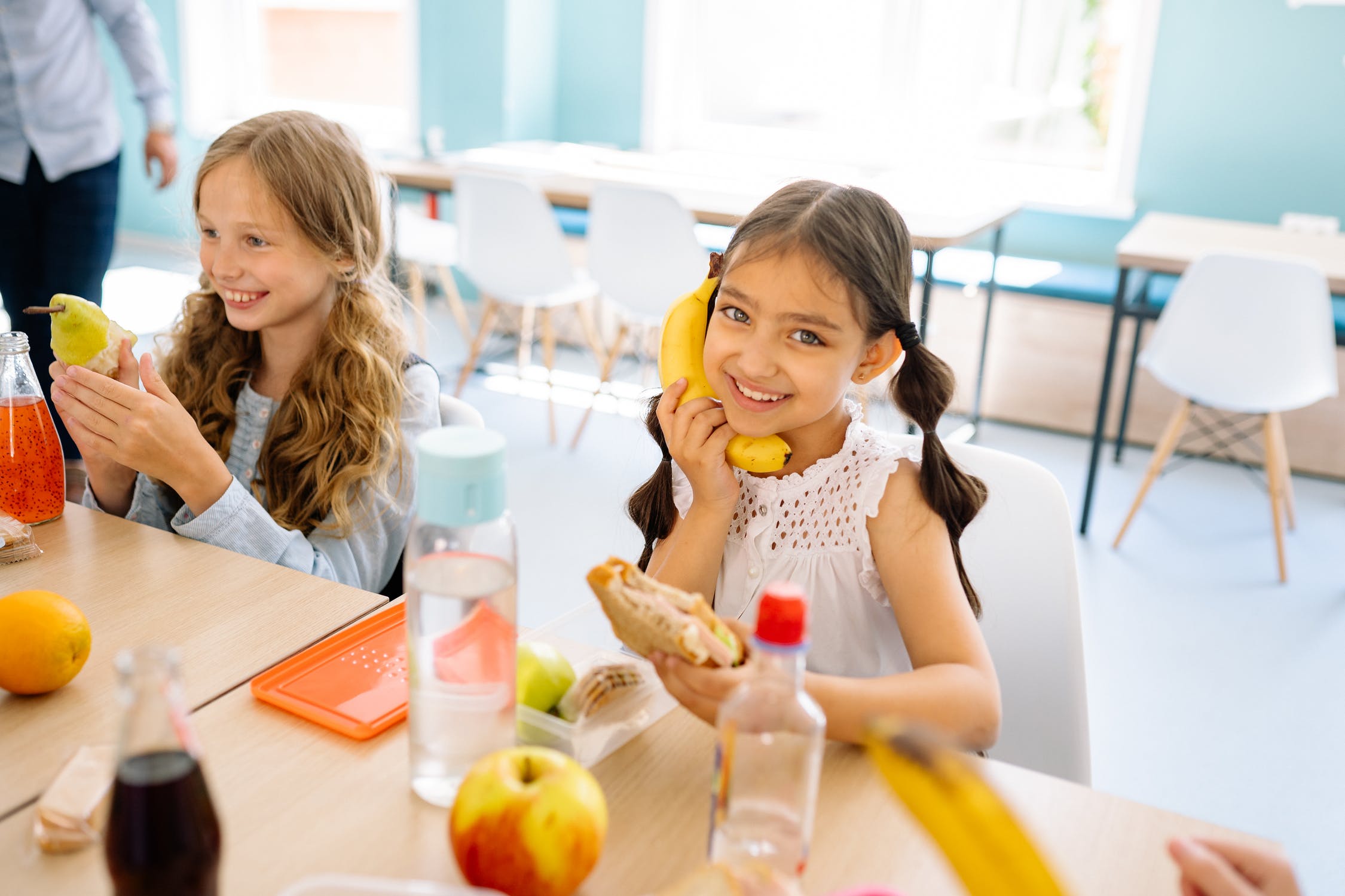 Zwei lachende Mädchen die Frühstückspause in der Schule haben. Links, blonde Haare und eine Birne in der Hand. Rechts, braune Haare und eine Banane wie ein Telefon am Ohr gehalten. 

#zcatering #caterer #berlin #kitacaterer #schulcaterer #regional #qualitativ #gesund #biocaterer #Mittagessen #Ernährung #ausgewogeneErnährung #Berlinmitte #BerlinerFamilienunternehmen 